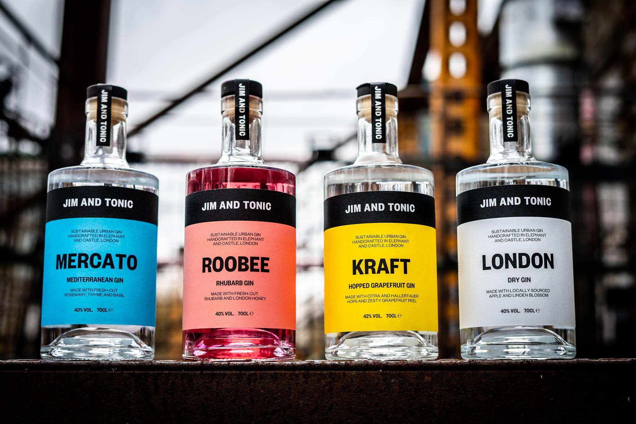 4 bottle of Jim and Tonic gin outside on a rusty looking metal surface with a blurred background of an urban setting.